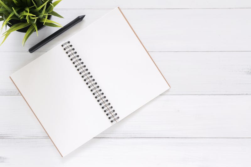 Cuaderno de espiral abierto en blanco con lápiz negro sobre mesa blanca