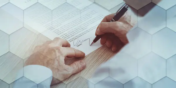 Manos firmando un documento legal con bolígrafo rojo sobre una mesa de madera