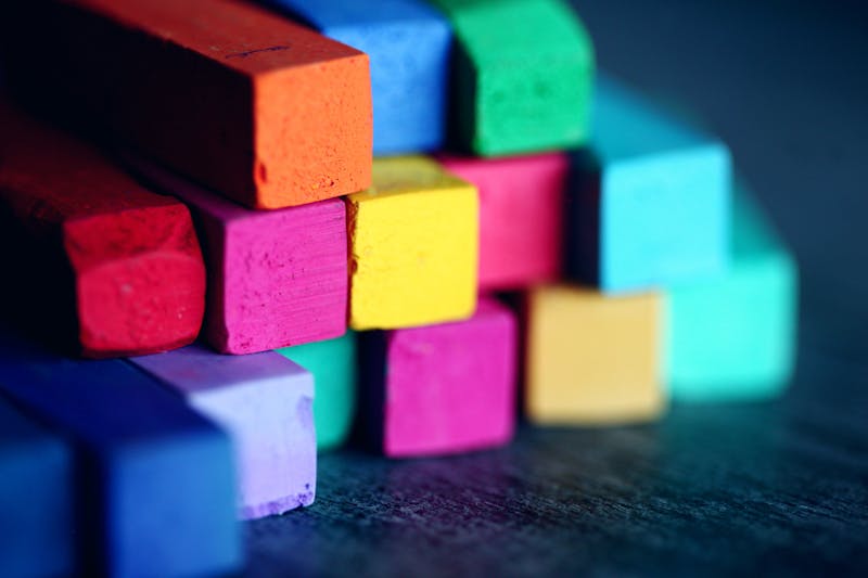 Bloques de tiza pastel de colores vivos —rojo, naranja, rosa, amarillo, verde, azul, morado— apilados en filas sobre superficie oscura