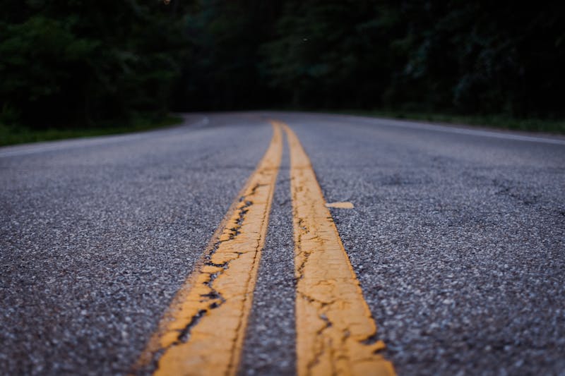 Carretera de asfalto con doble línea central amarilla que se adentra en un bosque al anochecer