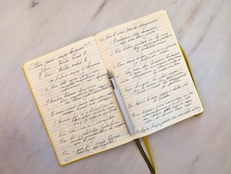 Cuaderno abierto sobre superficie de mármol con notas manuscritas en cursiva y un bolígrafo apoyado en las páginas
