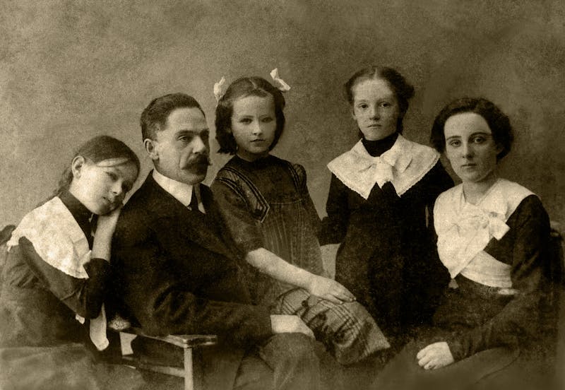 Retrato familiar sepia de principios del siglo XX, padre y madre con hijos en estudio fotográfico