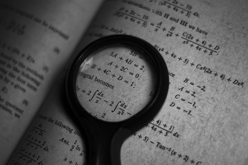 Lupa de aumento sobre una página de libro con ecuaciones matemáticas impresas en blanco y negro
