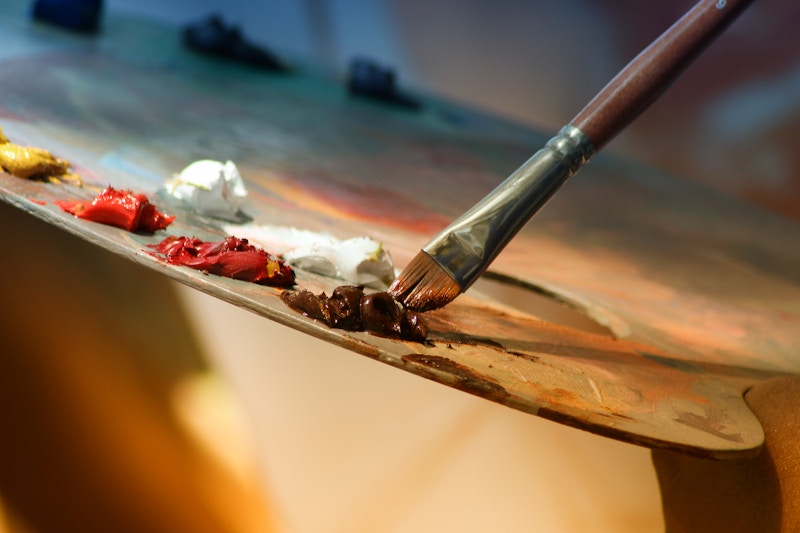 Paleta de pintor con manchas de pintura de múltiples colores sobre fondo de madera en un taller de arte