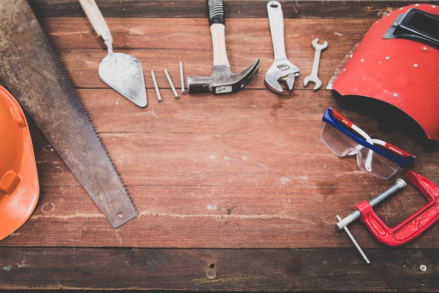 Conjunto de herramientas de construcción dispuestas sobre una mesa de madera: martillo, llave inglesa, sierra, casco