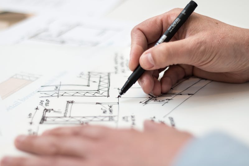 Mano dibujando planos arquitectónicos sobre papel con detalles técnicos