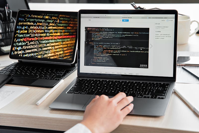 Programador trabajando con código en un portátil con varias pantallas en un escritorio moderno