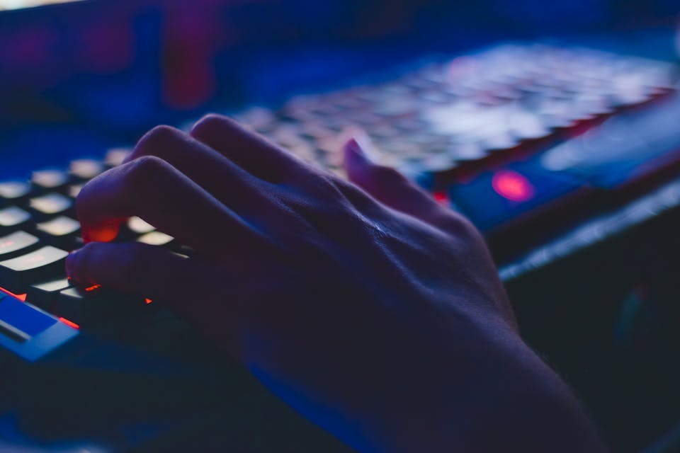 Teclado mecánico retroiluminado con código Python visible en pantalla de monitor al fondo