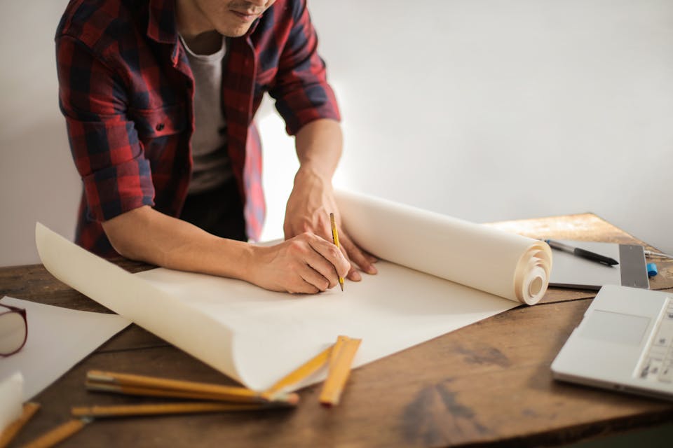 Arquitecto revisando planos técnicos detallados con escuadra y compás sobre mesa de trabajo