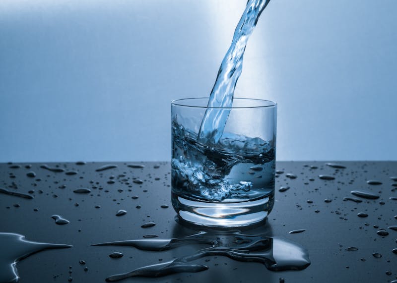Vaso de cristal con agua siendo vertida con fuerza, desbordándose sobre una superficie húmeda